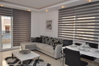 Alanya property living room featuring a modern sofa, dining area, and stylish horizontal blinds, creating a bright, airy atmosphere.