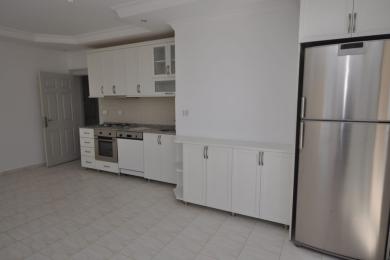 Cucina di proprietà ad Alanya con mobili bianchi, frigorifero in acciaio inossidabile, pavimenti piastrellati e atmosfera luminosa e ariosa.