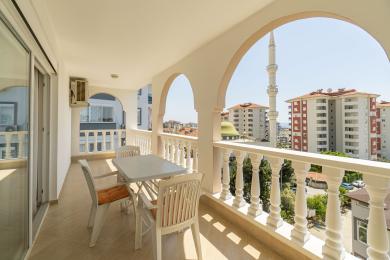 Varanda de propriedade em Alanya com arcos brancos, balaustrada, conjunto de jantar ao ar livre e vista da cidade, incluindo uma mesquita.