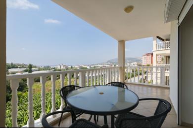 Alanya'da cam masa, hasır sandalyeler ve şehir manzaralı balkon.