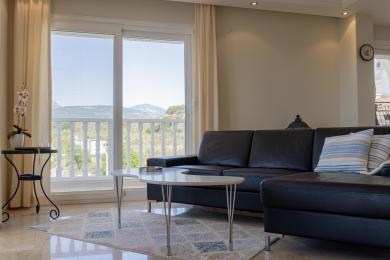 Alanijos svetainė su odine sofa, marmurinėmis grindimis ir balkono vaizdu į kalnus.