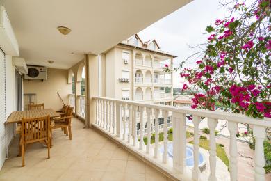 Alanya fastighet balkong med matgrupp i trä, vita räcken och bougainvillea med utsikt över trädgården.