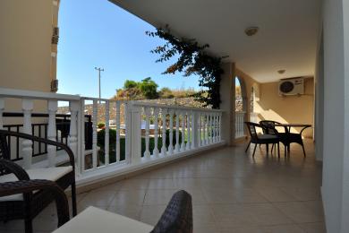 Alanya mulkidagi kafel qoplamali balkon, oq panjara, bog' manzarasi va tashqi o'tirish joyi.