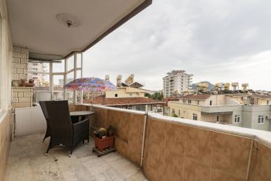 Balkon nekretnine u Alanji sa mermernim podom, nameštajem od pruća i pogledom na grad pod oblačnim nebom.