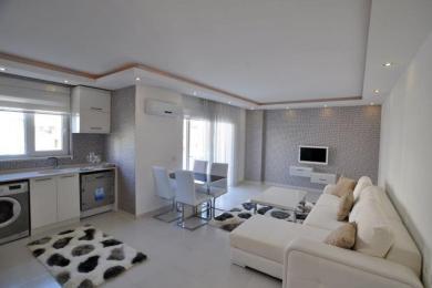 Alanja apartman dnevni boravak sadrži modernu kuhinju, trpezarijski set, teksturirani zid i udoban beli kauč.