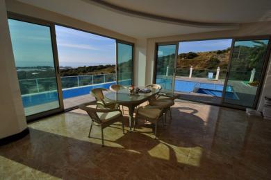 Die helle Sonnenterrasse der Immobilie in Alanya verfügt über einen Glastisch, Korbstühle, Marmorböden und Blick auf den Pool.
