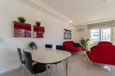 Lichte woonkamer in een appartement met moderne rode meubels, een eethoek en uitzicht op de stad door een groot raam.