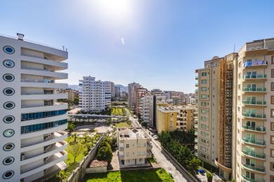 Alanya'da emlak manzarası: Parlak mavi gökyüzü altında balkonlu modern apartman binaları.