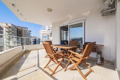 Alanya'da ahşap masa ve sandalyeli, mermer zeminli, parlak güneş ışığı alan ve şehir manzaralı balkon.
