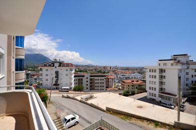 Vista del balcón de la propiedad de Alanya que muestra edificios de la ciudad, montañas y un ambiente brillante y soleado.