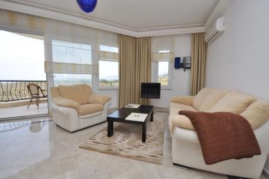 アランヤのリビングルームはバルコニーにアクセスでき、ニュートラルな色調、大理石の床、快適なシーティングが特徴で、明るく開放的な雰囲気を作り出しています。
