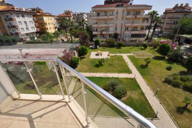 Alanya-Immobilienbalkon mit Glasgeländer bietet einen hellen Blick auf den angelegten Garten.