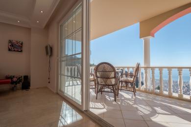 Alanya woning balkon met rieten stoelen, marmeren vloeren en prachtig uitzicht op zee, waardoor een ontspannen sfeer ontstaat.