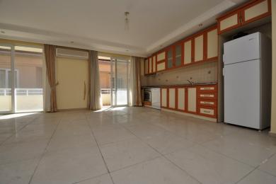Lyst Alanya køkken med flisegulv, orange og creme farvede skabe og adgang til balkon, hvilket skaber en rummelig fornemmelse.