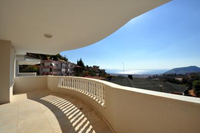 Alanya-Immobilienbalkon mit Marmorböden, weißer Balustrade und atemberaubendem Meerblick unter hellem Sonnenlicht.