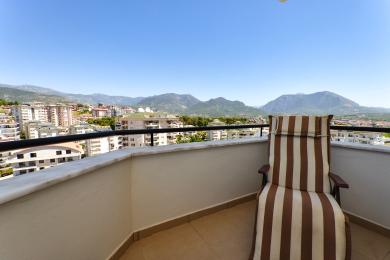 Alanya'da çizgili sandalyeli balkon, parlak ve güneşli bir günde muhteşem dağ ve şehir manzaraları sunuyor.