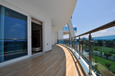 Balcon de propriété à Alanya avec revêtement de sol en carrelage imitation bois, garde-corps en verre et ambiance lumineuse et ensoleillée.