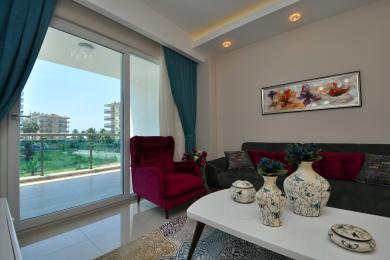 Yorug' Alanya mehmonxonasi balkon bilan, yumshoq kreslo, zamonaviy divan va neytral dekorga ega.