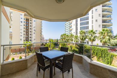 Balcon de propriété à Alanya avec mobilier en osier, balustrade en verre et vue ensoleillée sur la ville.