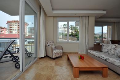 Alanya daş döşəməli, çiçəkli divanlı və eyvana çıxışı olan, parlaq və havadar bir atmosfer yaradan yaşayış otağı mülkü.