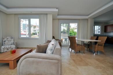 Luminoso soggiorno ad Alanya con pavimenti in travertino, divano neutro, set da pranzo in vimini e accesso al balcone.