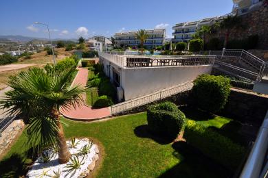 Die Immobilie in Alanya bietet eine üppige Landschaftsgestaltung, einen roten Backsteinweg und eine sonnige Dachterrasse mit Sitzgelegenheiten im Freien.
