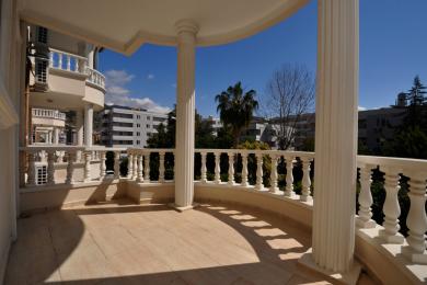 Varanda luminosa em Alanya com piso de mármore, grades brancas ornamentadas e colunas clássicas que oferecem vistas da cidade.