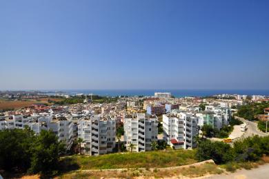 Uitzicht op een woning in Alanya met de skyline van de stad en de Middellandse Zee onder een helderblauwe hemel.