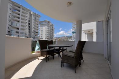 Balcon d'une propriété à Alanya avec des meubles en osier, un revêtement de sol en carrelage et une atmosphère lumineuse et aérée donnant sur la ville.