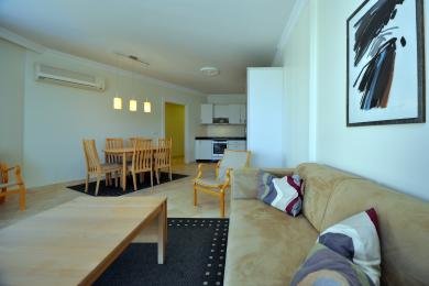 Apartamentul din Alanya are o zonă de luat masa, o bucătărie deschisă și o canapea bej confortabilă, cu lumină naturală.