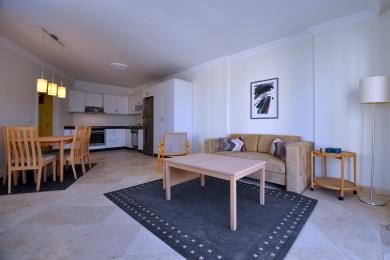 A világos alanyai apartman nappalija modern konyhával, kényelmes kanapéval és világos fa bútorokkal rendelkezik márványpadlón.