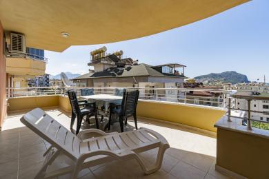 Zonnig Alanya appartement balkon met een lounge stoel en een eethoek met een prachtig uitzicht op de stad en de bergen.
