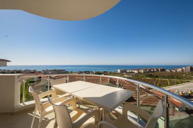 Alanya-Balkon mit Plastikmöbeln und atemberaubendem Meerblick, gebadet in hellem Sonnenlicht, wodurch eine entspannende Atmosphäre entsteht.