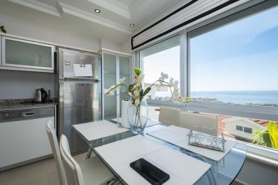 Helle Alanya Küche mit Edelstahlgeräten, Glastisch und Panoramablick auf das Meer, die eine moderne, luftige Atmosphäre schafft.