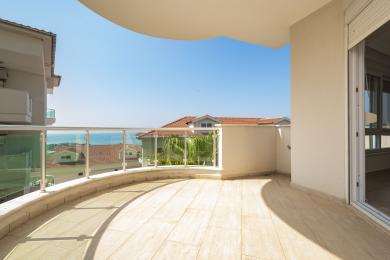 Svetli balkon u Alanji sa staklenom ogradom, podom od pločica i zadivljujućim pogledom na more pod vedrim plavim nebom.