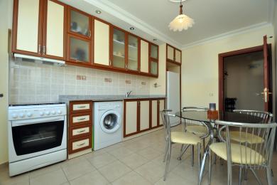 Bucătărie într-o proprietate din Alanya, cu dulapuri crem și din lemn, backsplash cu faianță și o masă de sufragerie cu blat de sticlă, creând un spațiu luminos și funcțional.