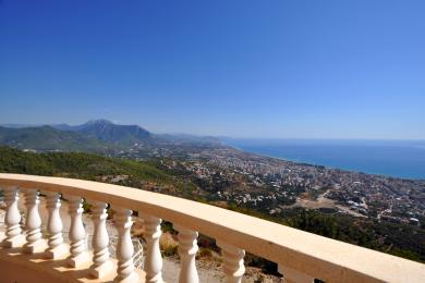 Alanya property balcony with white balustrade offers panoramic views of the city, mountains, and Mediterranean Sea.