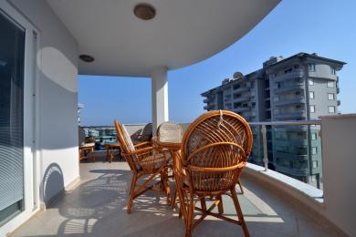Balconul proprietății din Alanya are mobilier din răchită, podele din gresie, lumină naturală strălucitoare și vedere la oraș, creând o atmosferă relaxantă.