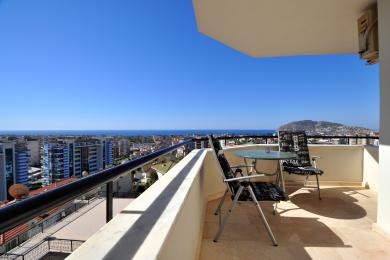 Alanya property balcony with city and sea views, featuring outdoor seating and bright, natural light.