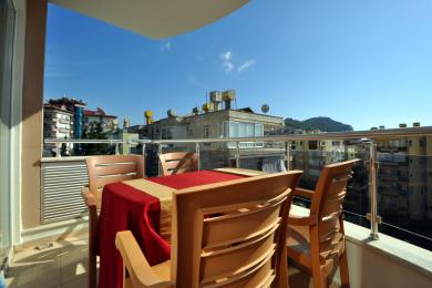 Alanya property features a balcony with an outdoor dining set, bright sunlight, and clear city views.