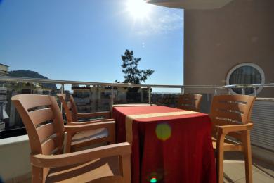 A bright balcony in Alanya features a table with a red cloth and wooden chairs, offering sunny outdoor living.