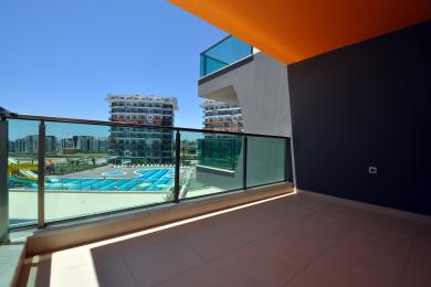 Alanya property balcony with glass railings offers bright views of the pool and nearby buildings.