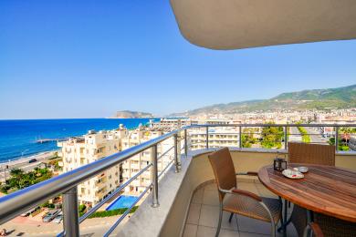 Balcone di proprietà ad Alanya con tavolo in legno, sedie in vimini e splendide viste sull'oceano e sulle montagne.