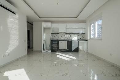 Lichte Alanya appartement keuken met moderne witte kasten, donkere werkbladen, marmeren vloeren en veel natuurlijk licht.