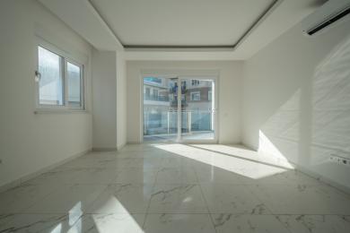 Een heldere, lege kamer in een appartement in Alanya met marmeren vloeren, witte muren en toegang tot het balkon, wat een modern en luchtig gevoel creëert.