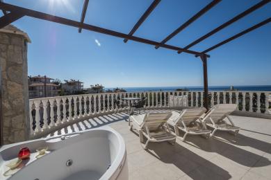 Den solfylte balkongen til Alanya-eiendommen har boblebad, loungestoler og fantastisk havutsikt under en pergola i tre.