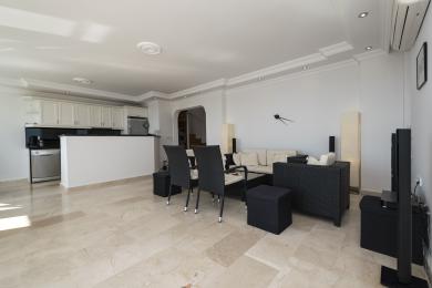 Sala de estar luminosa do apartamento em Alanya com cozinha aberta, pisos de mármore e móveis modernos em preto e branco.