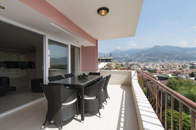 Balcone di proprietà ad Alanya con set da pranzo in vimini, pavimento in piastrelle e vista panoramica sulla città e sulle montagne.