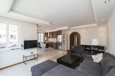 Alanya property: Open-plan living room with kitchen, featuring tile floors, recessed lighting, and comfortable gray seating.