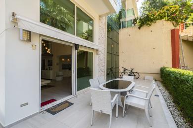 Patio nekretnine u Alanji s bijelim namještajem od pruća, podovima od mramora i kliznim staklenim vratima koja vode u svijetli interijer.